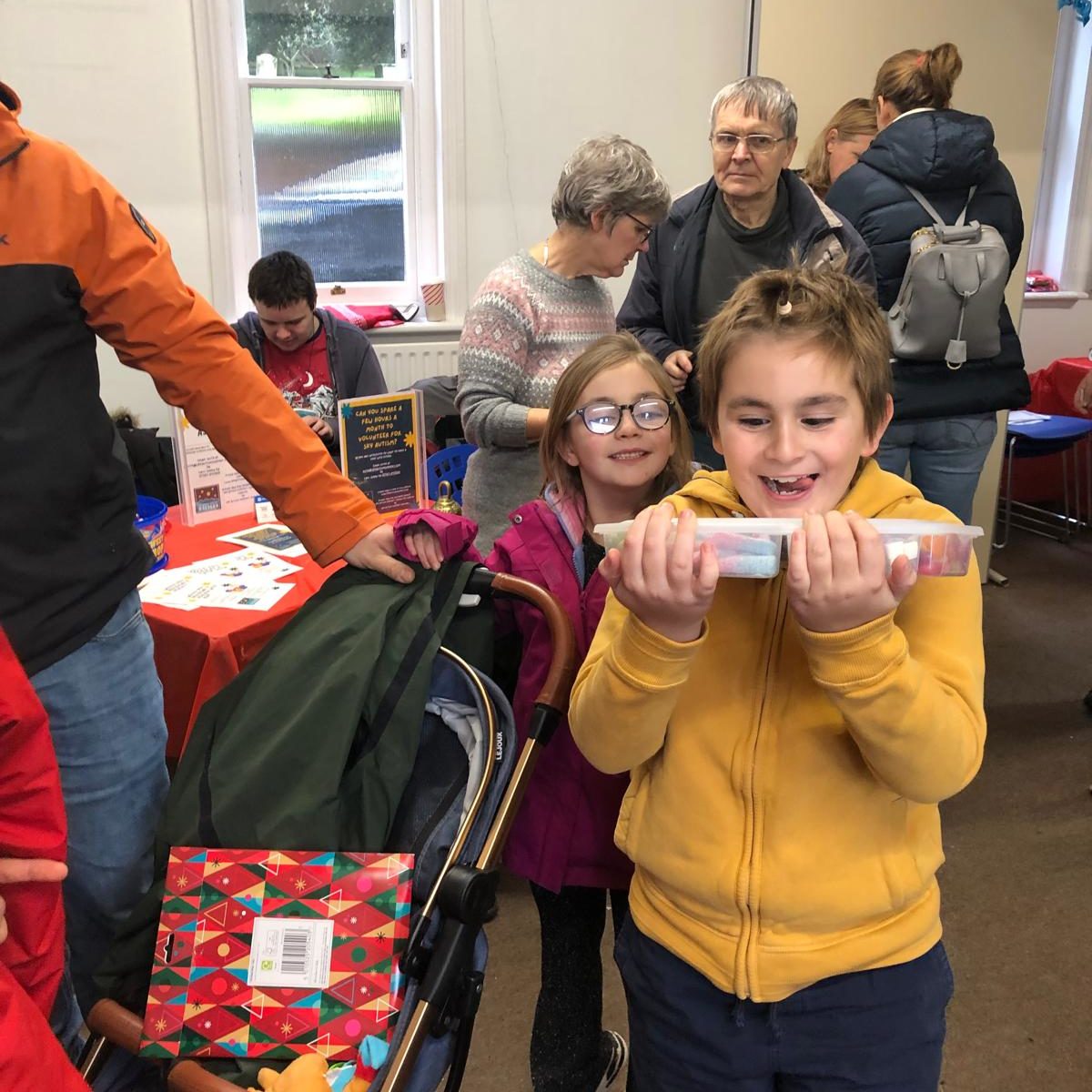 Children and adults stand around a tombola stall, joyfully displaying a tombola prize they have won.